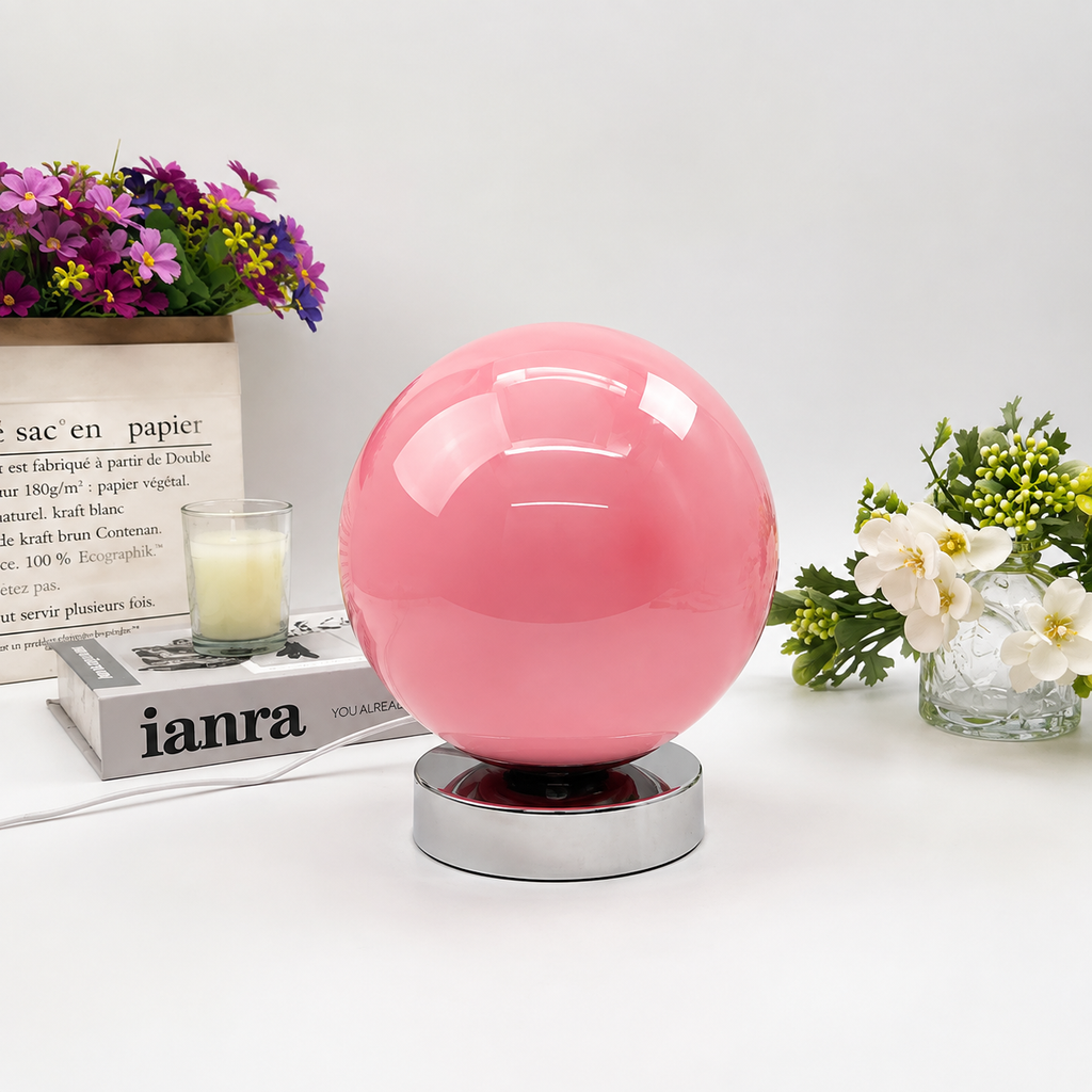 Globe table lamp, pink blown-glass shade on a polished chrome base, on a white table