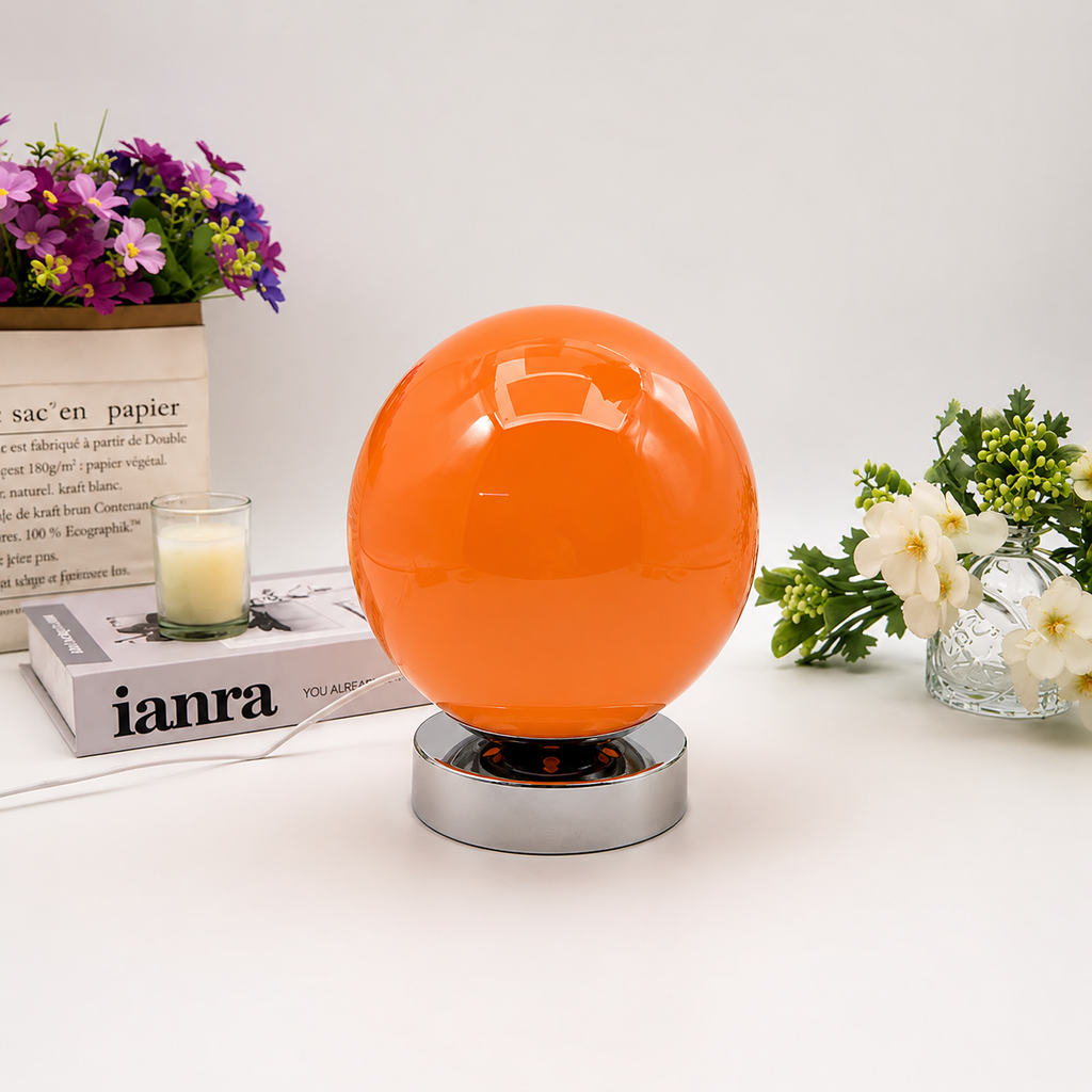 Orange Globe table lamp shown from the front beside flowers and books