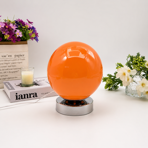 Orange Globe table lamp shown from the front beside flowers and books