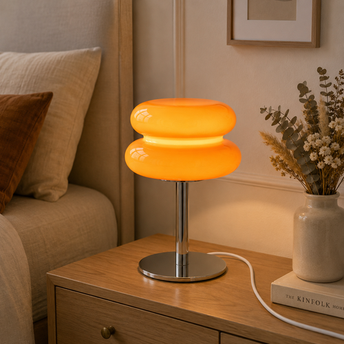 Orange Macaron lamp lit on a bedside table, casting a warm amber glow