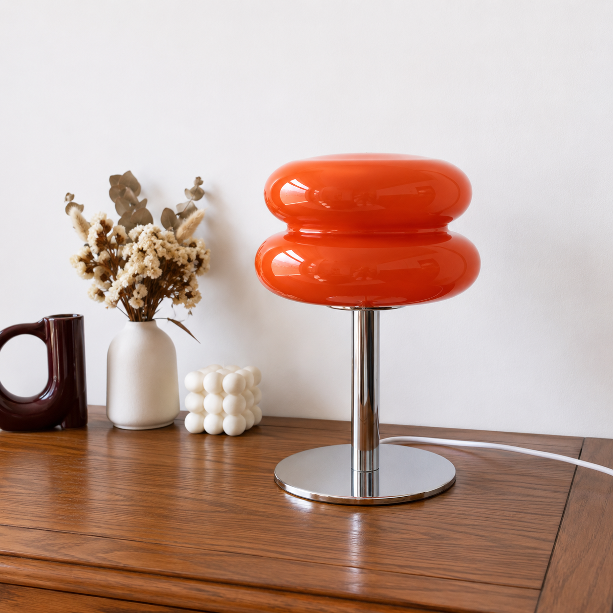 Red Macaron glass lamp on a walnut sideboard beside dried flowers